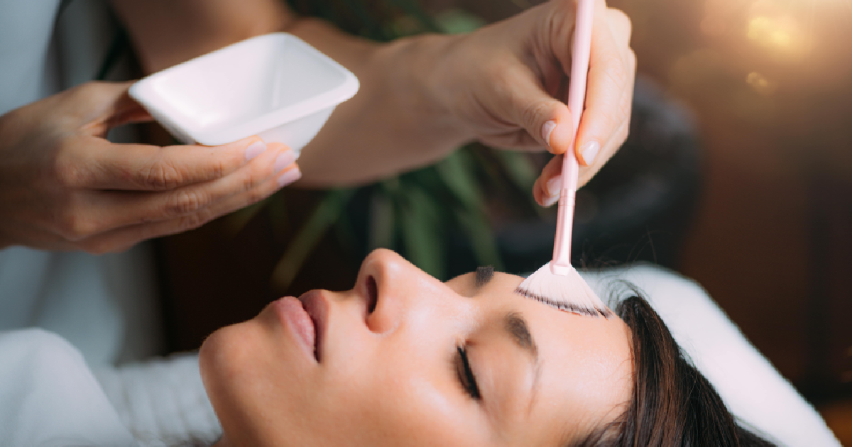 Woman receiving a facial peel treatment with a brush applicator on her forehead in a professional skincare in Texas